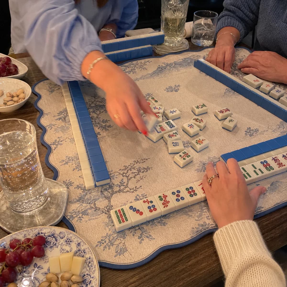 Hands playing American Mahjong on a blue botanical mat